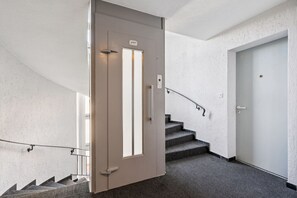 A modern interior with a staircase, a door with a handle, and a wall-mounted light fixture.