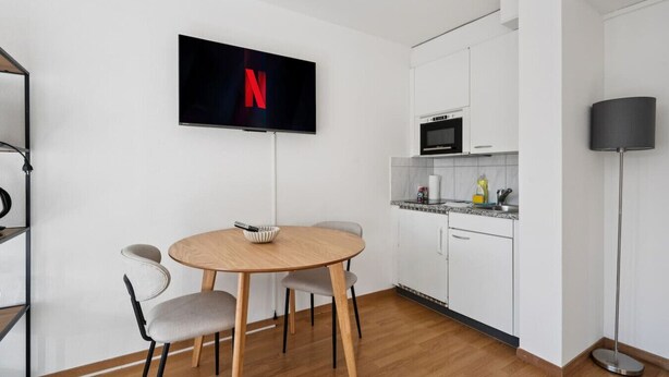 Eine moderne Küche mit weißen Schränken, einer Mikrowelle und einem flachbildfernseher an der Wand.