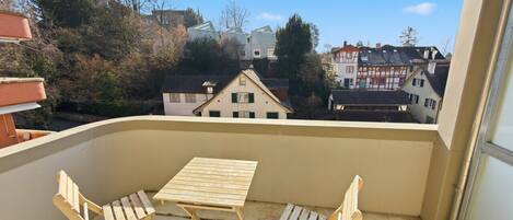 A balcony with a table and two chairs, overlooking a residential area with houses.
