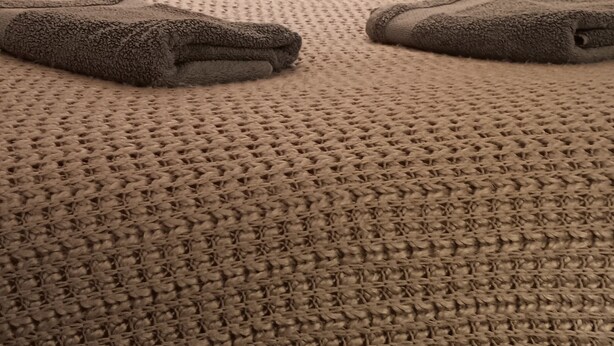 A bed with a textured blanket, two pillows with a polka dot pattern, and a dark headboard.