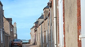A narrow cobblestone street lined with historic buildings, a parked car, and a clear sky.