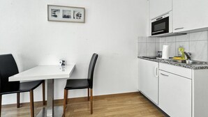 Una cocina moderna con armarios blancos, un microondas y un fregadero. Hay un cuadro en la pared y una mesa de comedor con dos sillas.