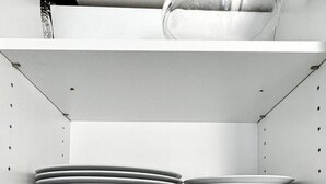 Una cocina con estantes blancos que sostienen platos, tazones y tazas.