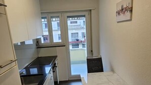 A compact kitchen with white cabinets, a black countertop, and a small dining table with a chair. - Cozy studio near train station (Wille 7) (Zürich)