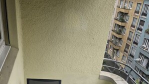 A balcony with a marble table and chairs, a yellow wall, and a view of a residential building. - Cozy studio near train station (Wille 7) (Zürich)
