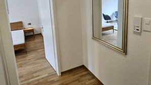 A narrow hallway with wooden flooring and white walls. A large mirror is mounted on the wall, and a door leads to another room. - Cozy studio near train station (Wille 7) (Zürich)