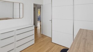 Una stanza con una cassettiera bianca, uno specchio, un tavolo in legno e un armadio.