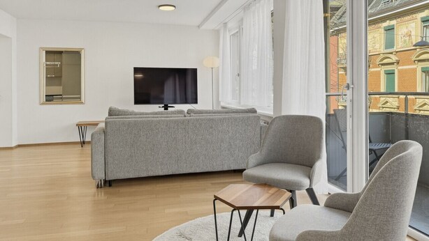 Un soggiorno moderno con un divano grigio, due poltrone, un tavolino da caffè e una TV.