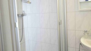 Een badkamer met een douchecabine van glas, witte betegelde wanden en een wastafel met spiegel erboven.
