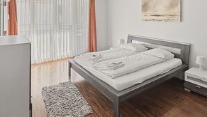 A modern bedroom with a bed, bedside tables, a nightstand, a window with curtains, and a painting on the wall. - 2BR near lake (Flower 23) (Zürich)