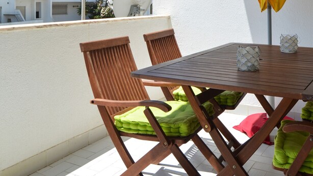 A balcony with a wooden table and chairs, a yellow umbrella, and a white building in the background. - BeGuest Feliz Choro (Albufeira)