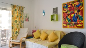 A room with a sofa, a rocking chair, a wicker chair, a painting, and a small green shelf. - BeGuest Feliz Choro (Albufeira)