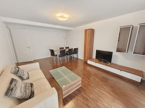 A modern living room with a sofa, coffee table, TV, and dining area.