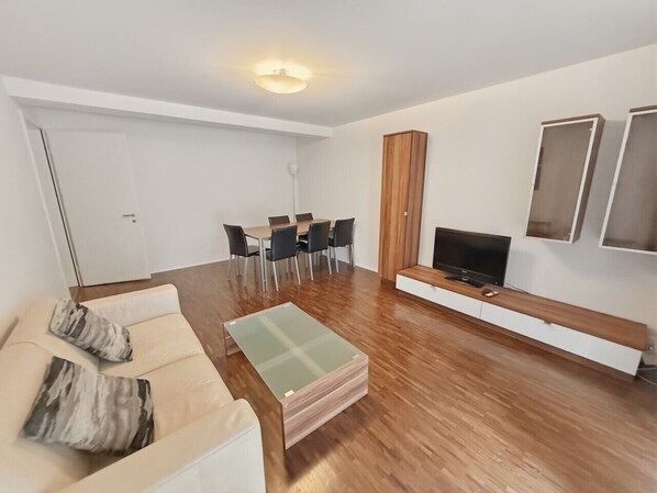 A modern living room with a sofa, coffee table, TV, and dining area.