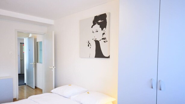 Een hotelkamer met een bed, nachtkastje, kledingkast en een schilderij aan de muur.