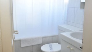 Een kleine, witte badkamer met toilet, wastafel en douchegordijn.