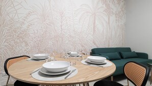 A dining area with a round table set for four, surrounded by chairs. A green sofa is against the wall.