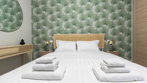 A neatly made bed with white linens and two folded towels at the foot of the bed.