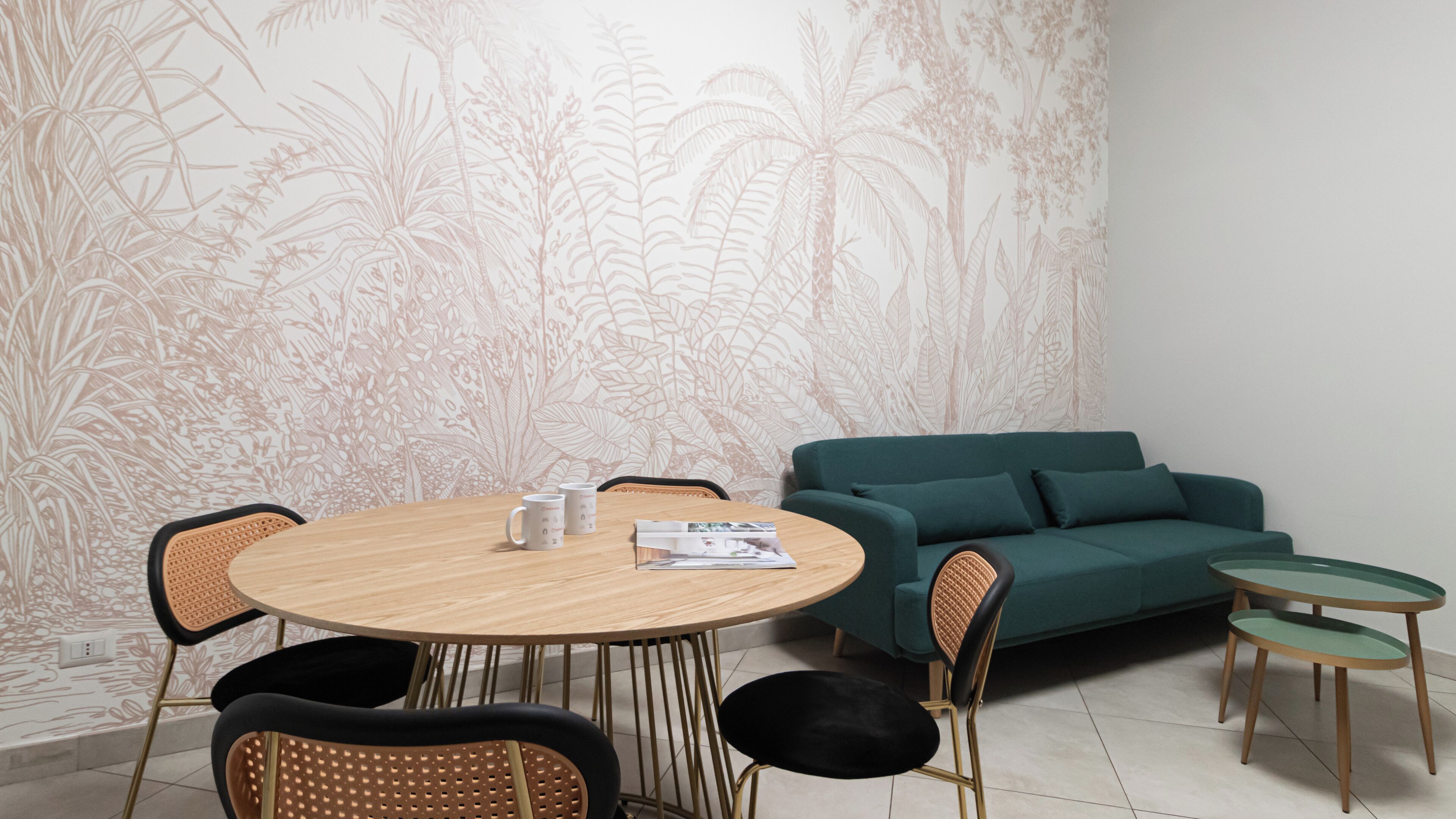 Un coin repas avec une table ronde en bois, des chaises noires et marron, un canapé turquoise et une petite table d’appoint.