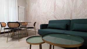 A living room with a green sofa, two round glass tables, and a dining area with a white table and chairs.