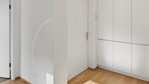 Ein Zimmer mit weißen Wänden, Holzboden, geschlossener Tür und einem Kleiderschrank mit vielen Fächern.