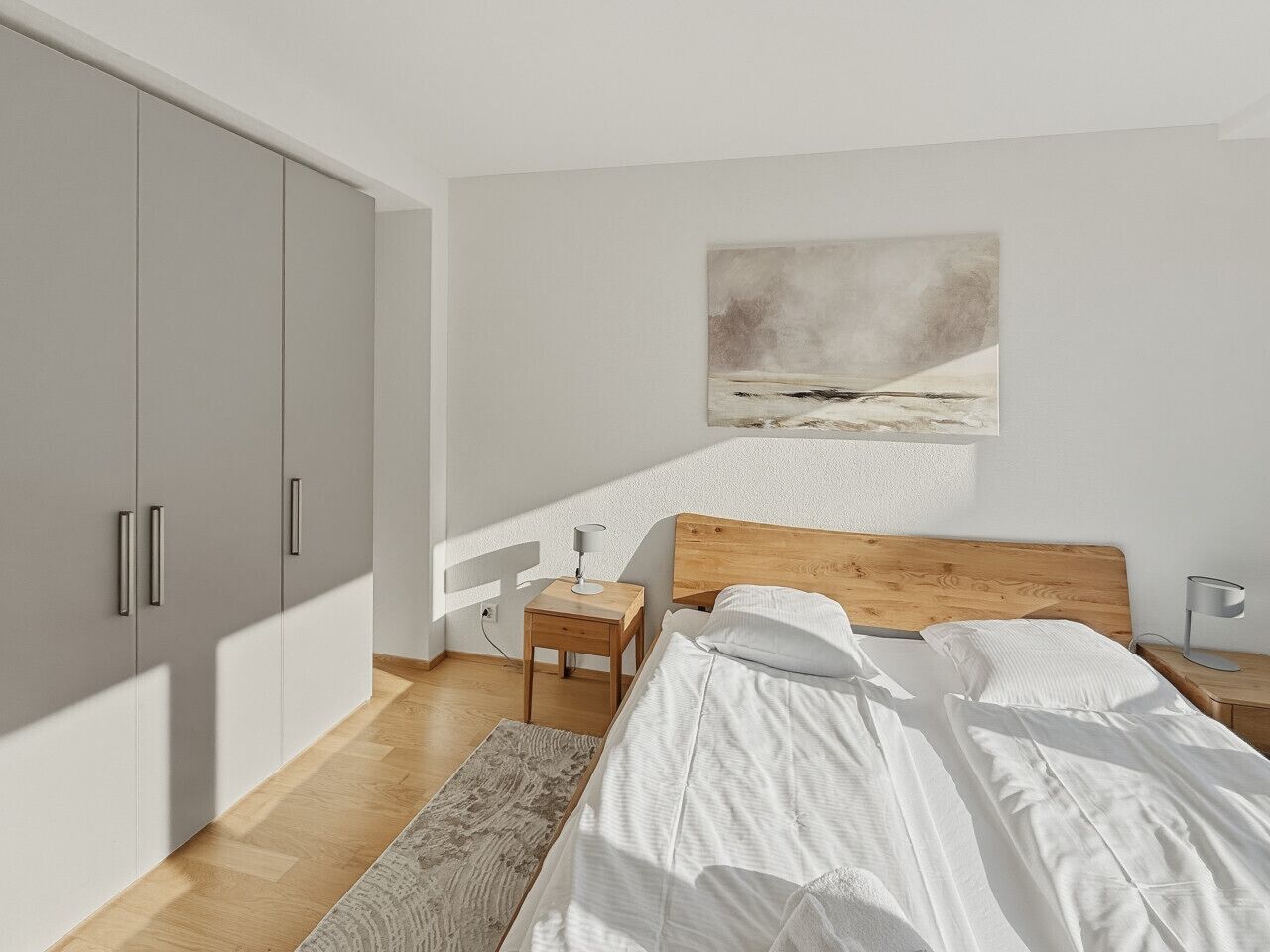 Ein Schlafzimmer mit einem Bett, einem Holzkopfende, Nachttischen, einem Beistelltisch, einem großen Kleiderschrank, einem Bild an der Wand und einem Teppichboden.