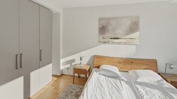 Ein Schlafzimmer mit einem Bett, einem Holzkopfende, Nachttischen, einem Beistelltisch, einem großen Kleiderschrank, einem Bild an der Wand und einem Teppichboden.