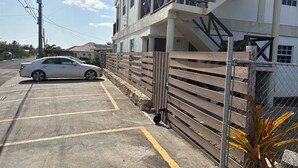Un espace de stationnement avec une voiture, un bâtiment doté d’un balcon et une clôture.