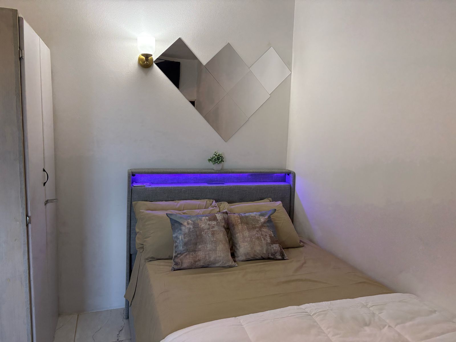 A bedroom with a bed, a wall-mounted mirror, and a blue under-bed lighting.
