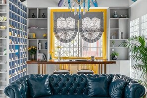 A room with a blue leather sofa, a wooden desk, and a large window with decorative glass panels. - Your City Pinghua Impression Inn (Kunshan)