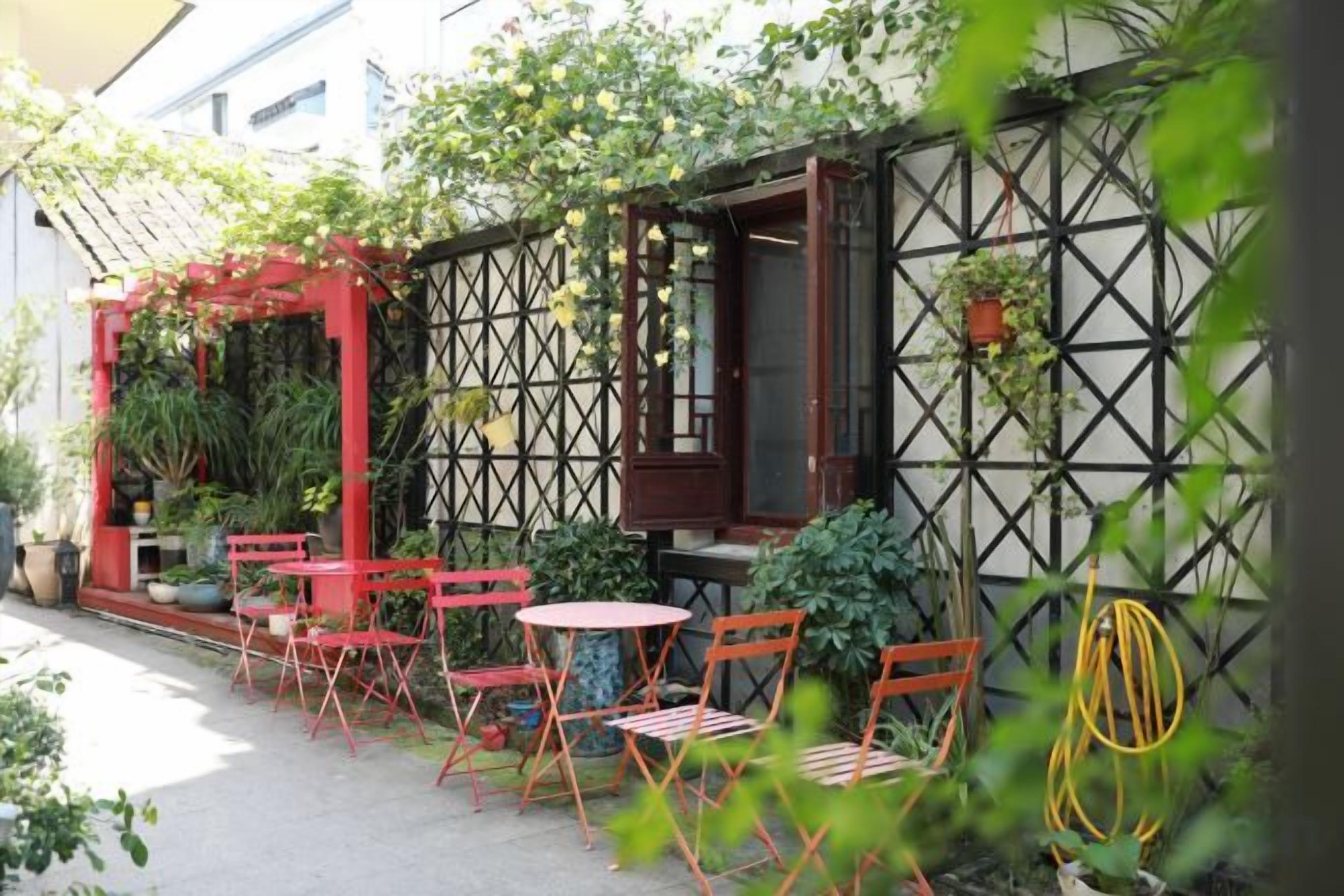 An outdoor seating area with tables and chairs, surrounded by plants and a lattice wall.