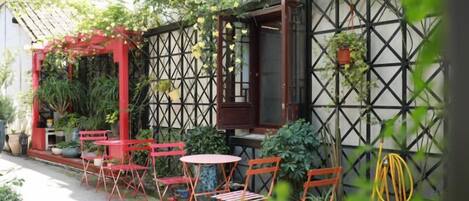 An outdoor seating area with tables and chairs, surrounded by plants and a lattice wall.