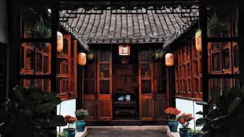 A traditional wooden structure with a tiled roof, potted plants, and hanging lanterns.