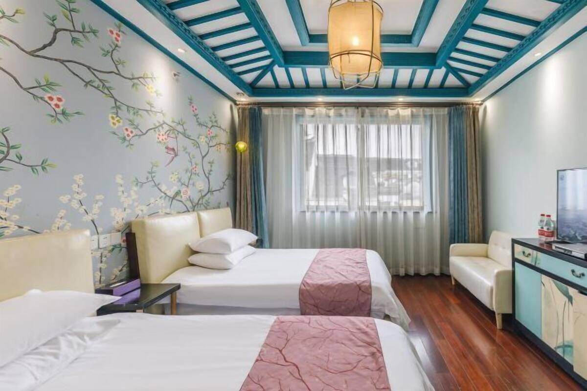 A hotel room with two beds, a sofa, a TV, and a window with curtains.