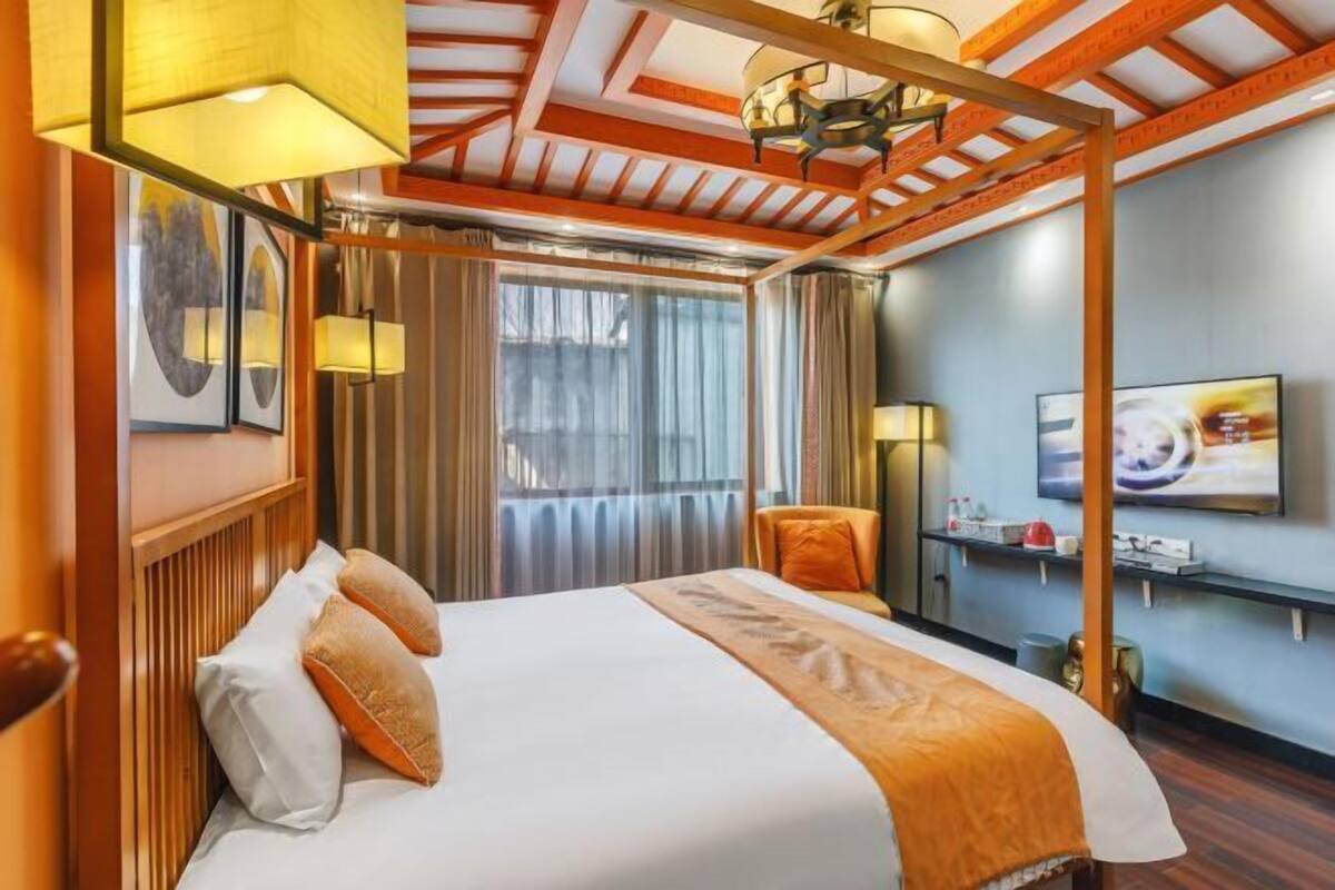A hotel room with a bed, a TV, a window with curtains, and a wooden ceiling.