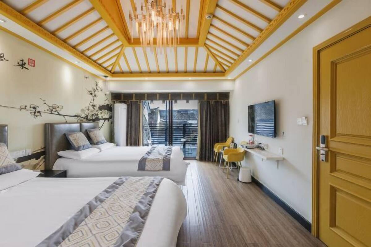 A hotel room with two beds, a TV, a chandelier, and a view of a building outside.