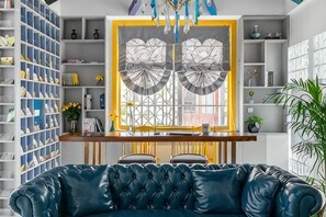A living room with a blue leather sofa, a wooden coffee table, and a large window with decorative glass panels. - Your City Pinghua Impression Inn (Kunshan)