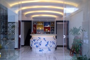 A reception area with a curved counter, glass partitions, and shelves with decorative items. - Your City Pinghua Impression Inn (Kunshan)