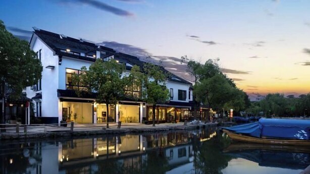 A waterfront property with a reflective pool, modern buildings, and a traditional-style boat docked nearby. - Your City Pinghua Impression Inn (Kunshan)