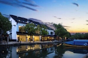 A waterfront property with a reflective pool, modern buildings, and a traditional-style boat docked nearby.