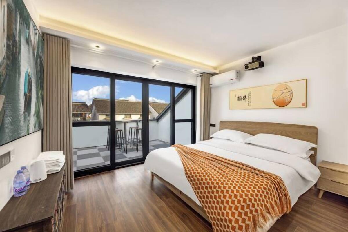 A modern hotel room with a large bed, a desk, and a balcony with a view.