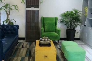 A room with a blue sofa, a green armchair, a yellow ottoman, and a potted plant.