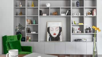 Una habitación con una estantería gris, un sillón verde, un ordenador portátil, un jarrón con una flor amarilla y una obra de arte enmarcada.