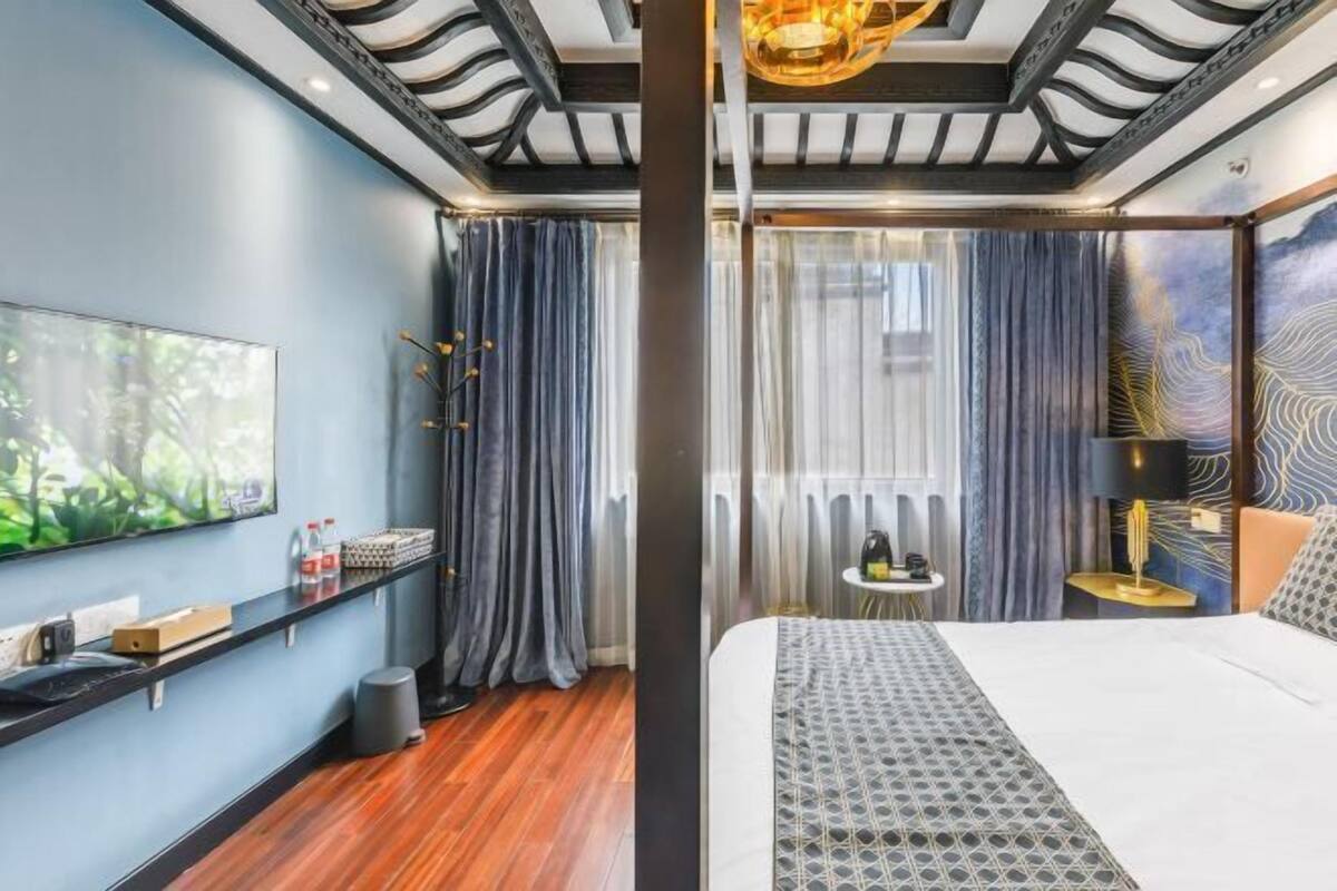 A modern hotel room with a large bed, a flat-screen TV, a small side table, and a view of the outdoors.