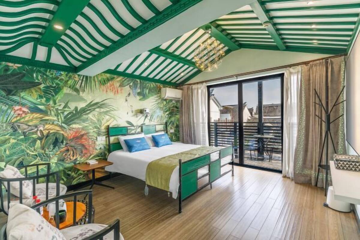 A bedroom with a bed, a mural, a balcony, and a view of the outside.