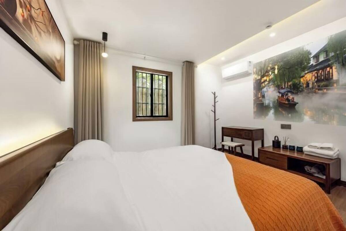 A hotel room with a bed, a desk, a chair, a window, and a wall-mounted artwork.