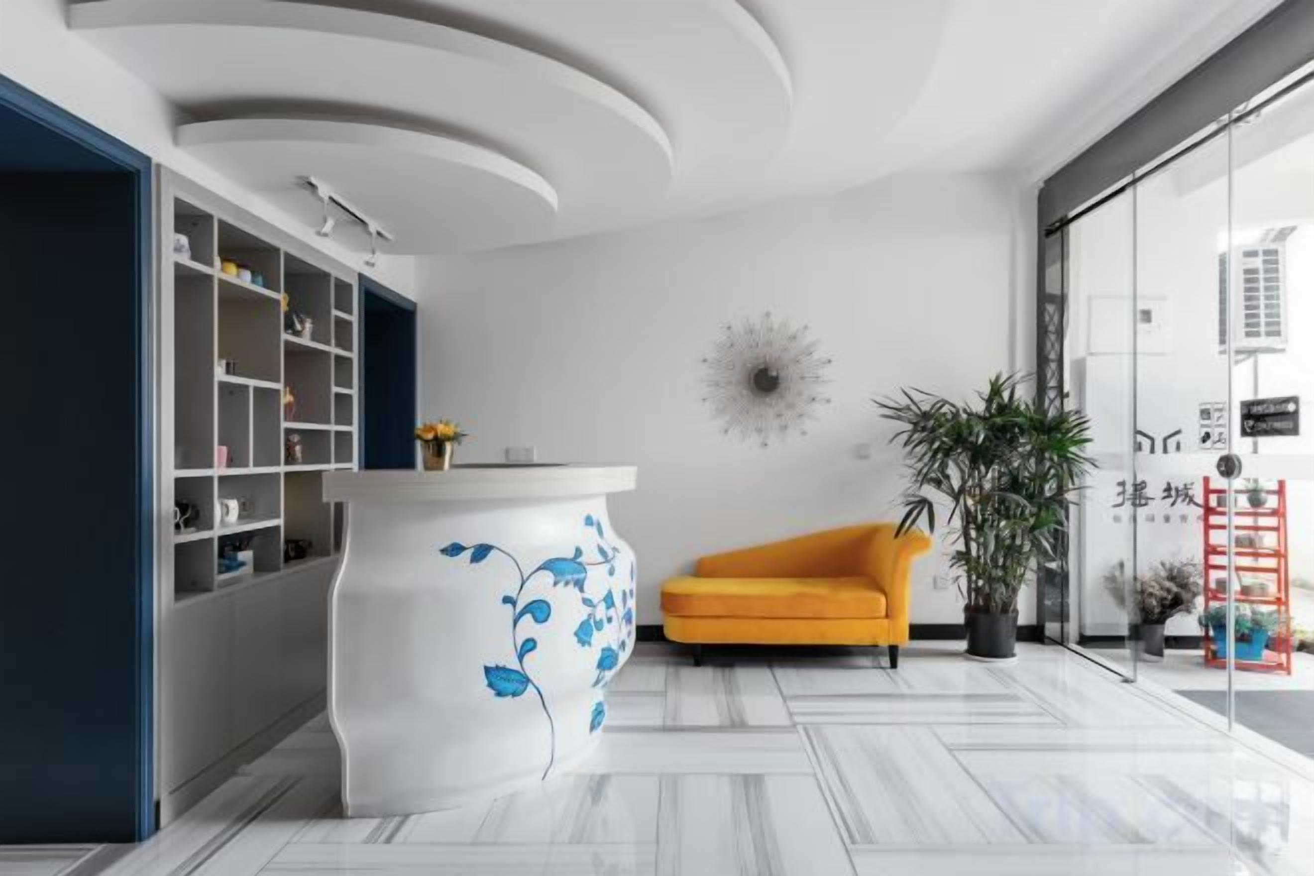 A modern interior with a white reception desk, a yellow armchair, and a large potted plant.