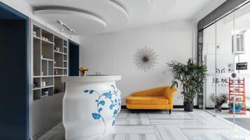 A modern interior with a white reception desk, a yellow armchair, and a large potted plant.