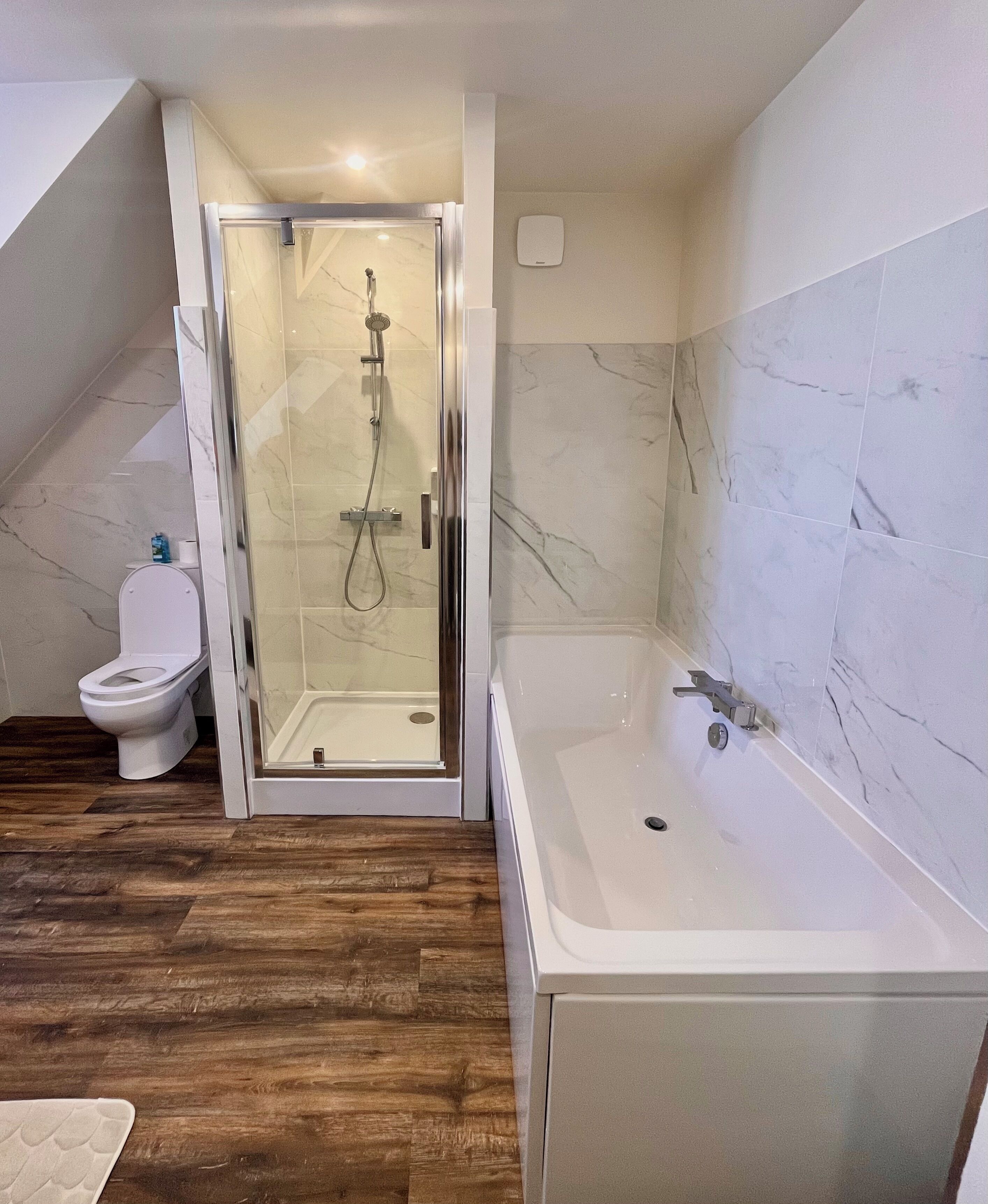 Un baño con ducha envuelta en vidrio, inodoro blanco y bañera.