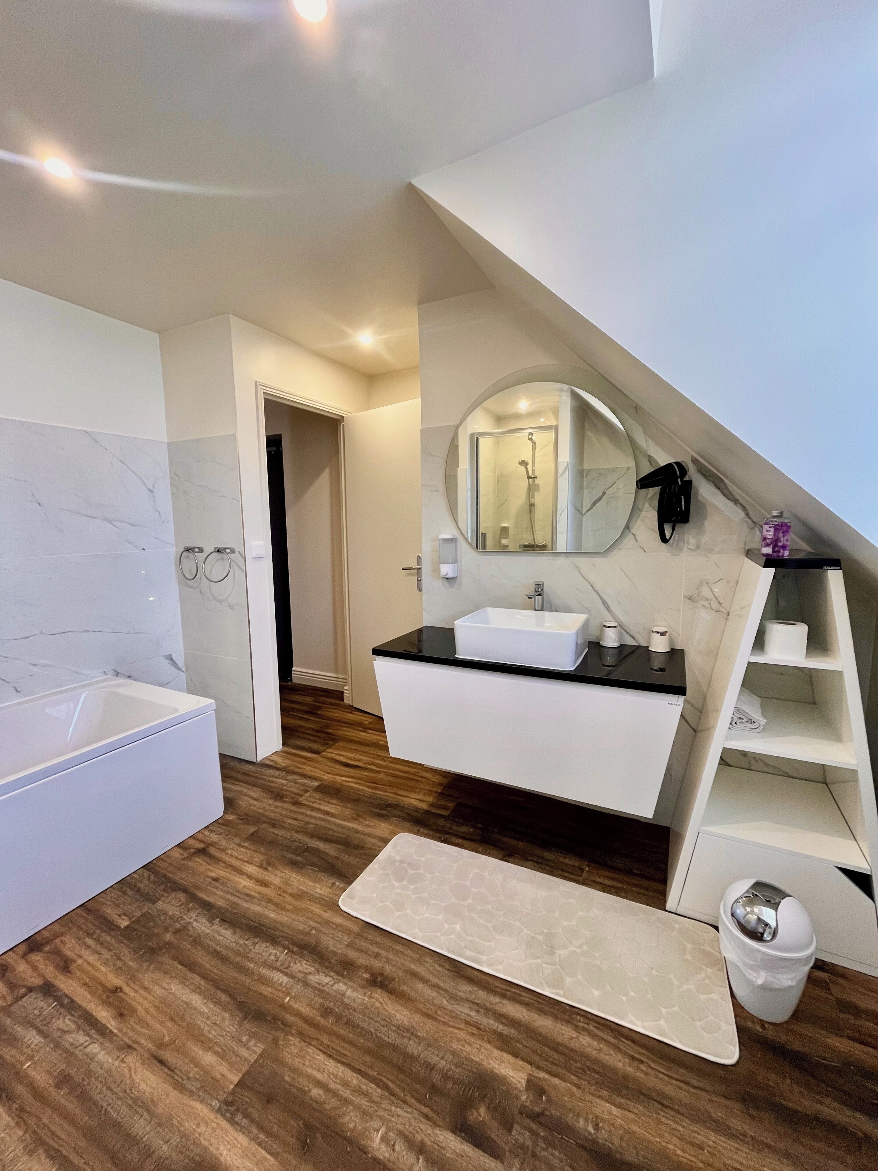 Une salle de bain moderne équipée d’une baignoire, d’un meuble-lavabo avec un évier, d’un miroir et d’une douche.